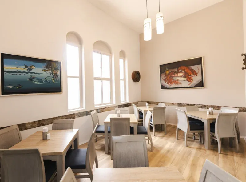 Comedor con cuadros de peces y langostas y ventanales arqueados en Pescocentro Búcaro, Bucaramanga